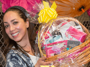A woman holds up a completed gift basket filled with bath and self-care products