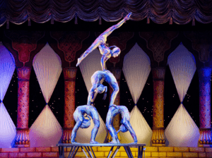 A group of four acrobats form a pyramid, with the acrobat on top doing the slips in a handstand position.