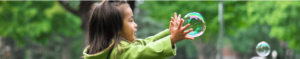 a young girl reaches out her arm to pop a soap bubble