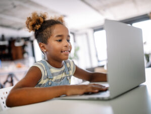 Child sitting at laptop, smiling.