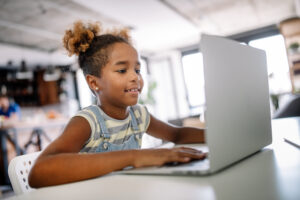 Child sitting at laptop, smiling.