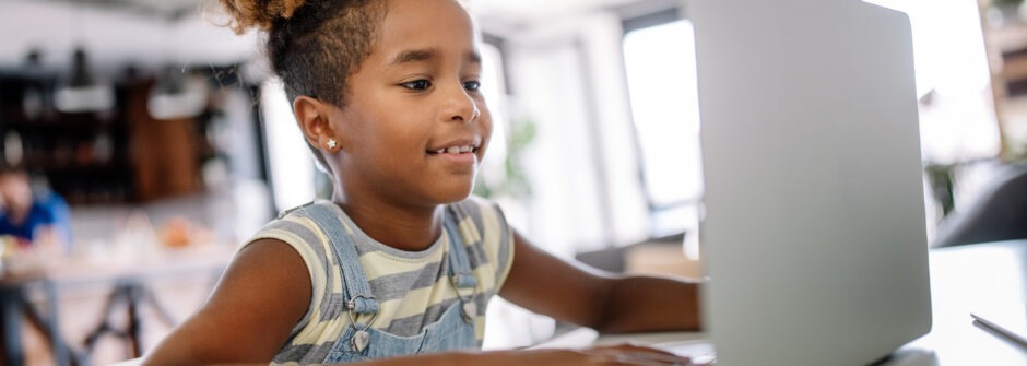 Child sitting at laptop, smiling.