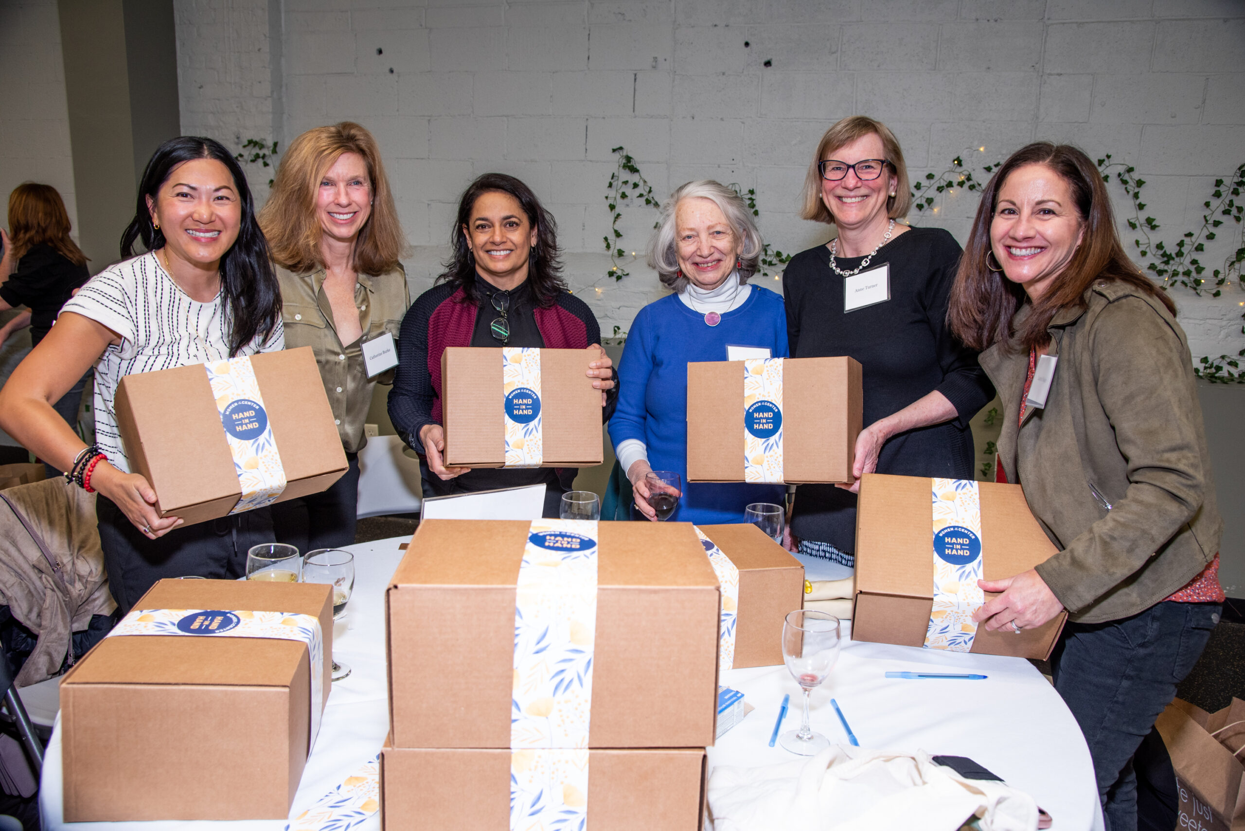 Women holding and standing with Hand in Hand care packages they assembled.